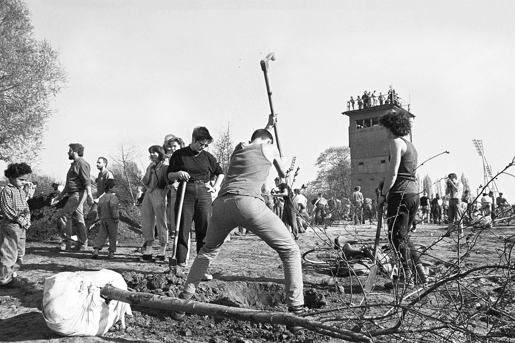 Workers plant trees for the newly developed Mauerpark. In the background, onlookers are standing on a former watchtower.