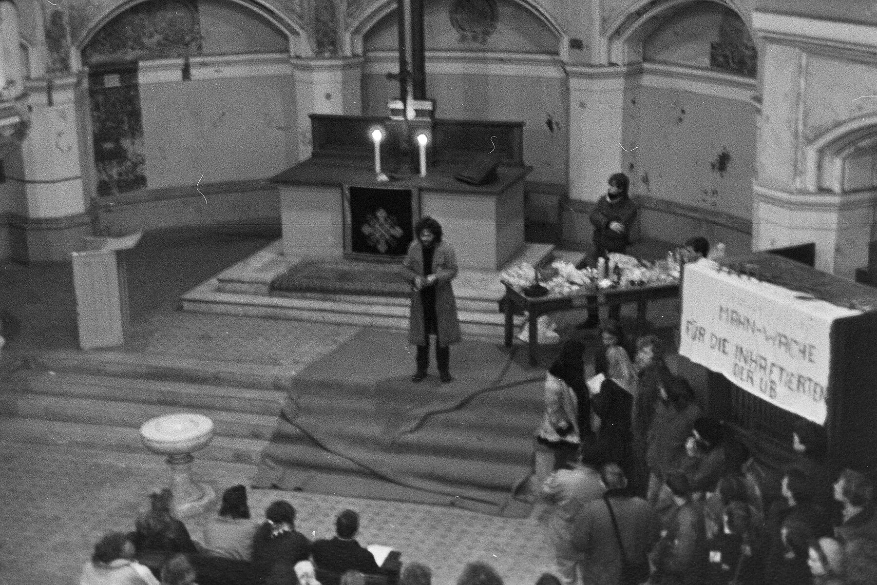 Mitglieder der Umweltbibliothek halten eine Mahnwache in der Zionskirche ab. Eine Person spricht vom Altar aus zu ihnen.