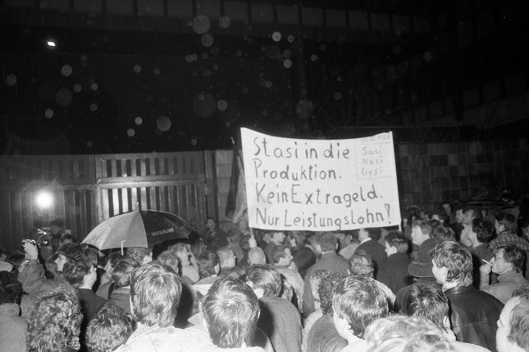 A crowd of people in front of the Ministry's building. A poster reads: Stasi into production. No extra money. Incentive wage only!