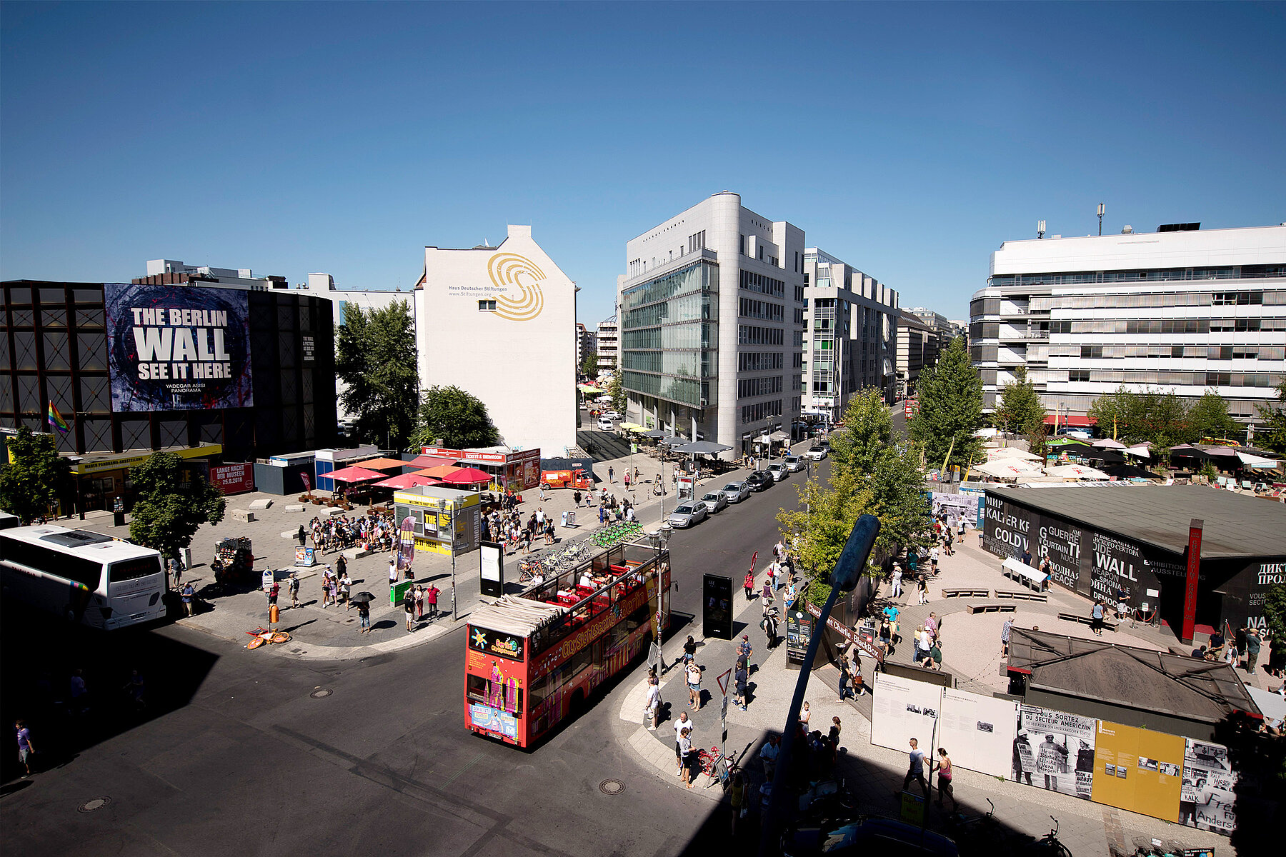 Luftaufnahme einer Straßenkreuzung und Freifläche. Rechts befinden sich Verkaufsstände, links die Black Box Kalter Krieg.