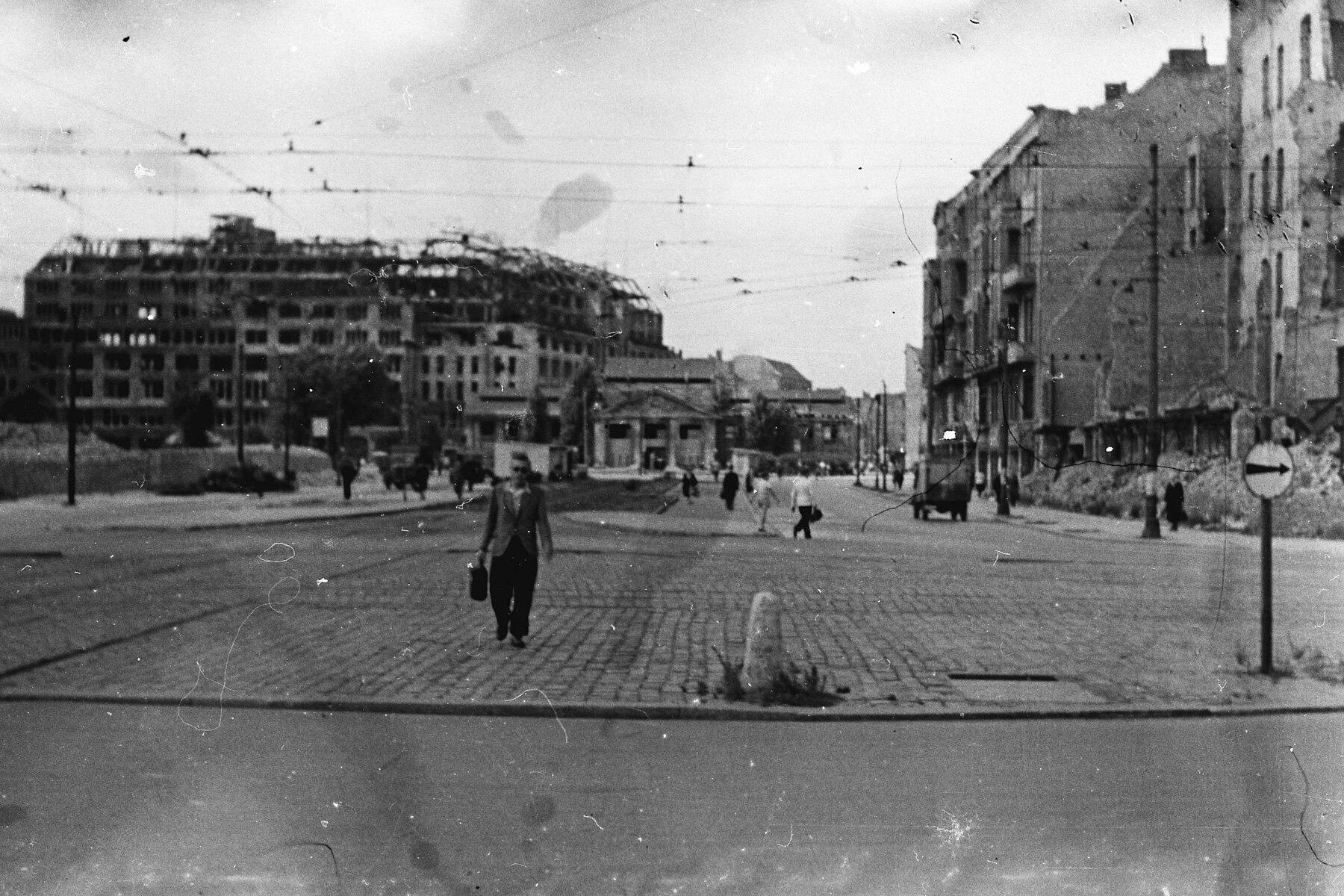 A cobbled square, on the left and right in the background are buildings damaged by bombs. 