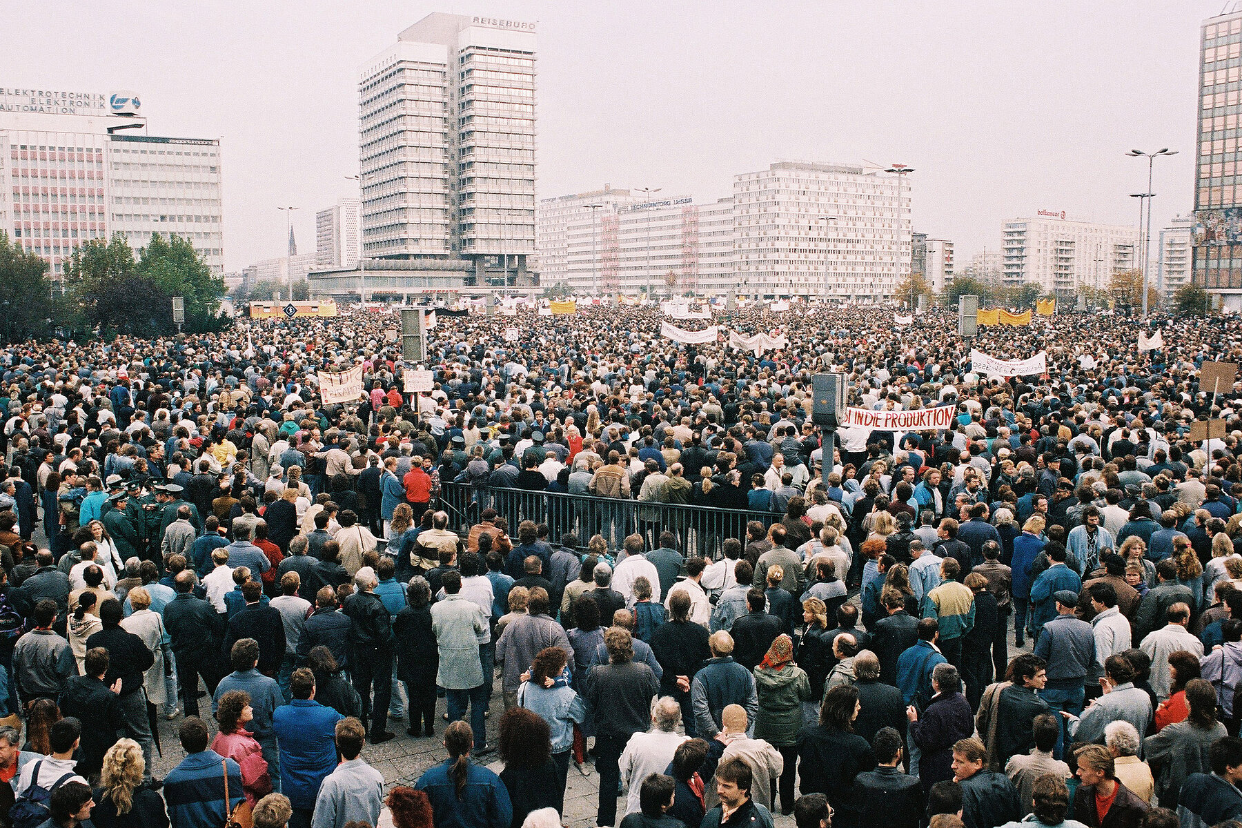 Eine Masse von Demonstrierenden ist auf dem Alexanderplatz in Ost-Berlin versammelt. Im Hintergrund befinden sich Hochhäuser.
