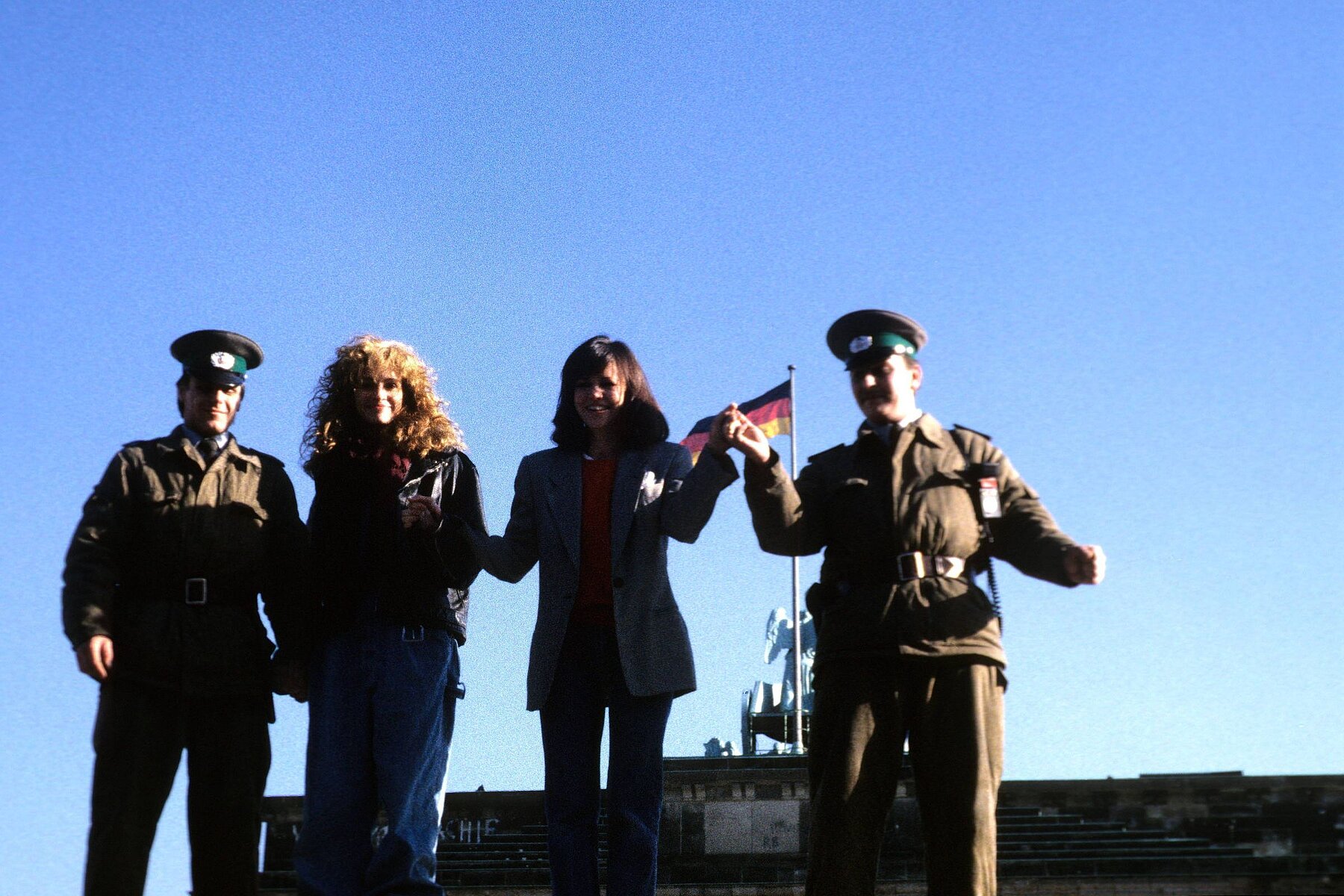 Actresses Julia Roberts and Sally Field pose with a GDR border soldier on the anti-tank wall at the Brandenburg Gate. 