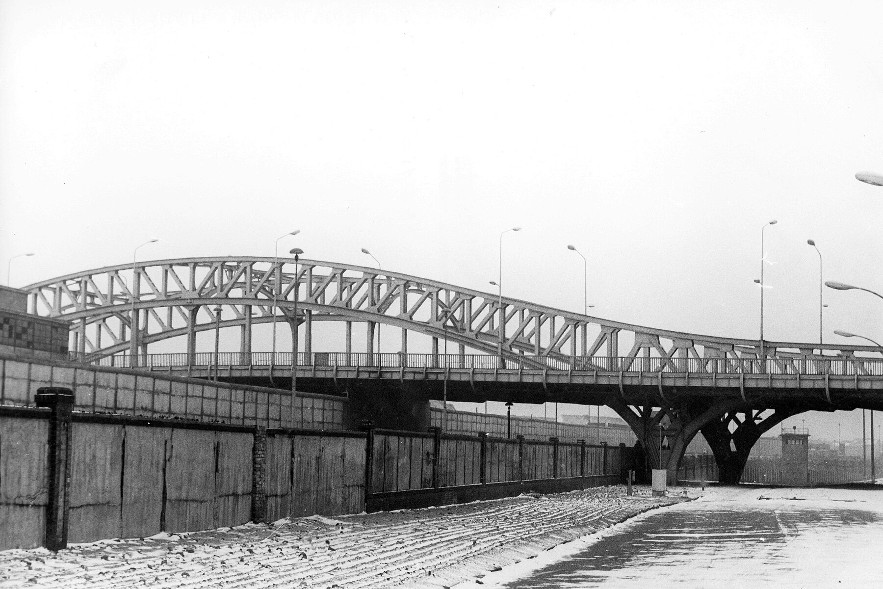 The Berlin Wall extends along the railroad tracks and underneath the Bösebrücke.
