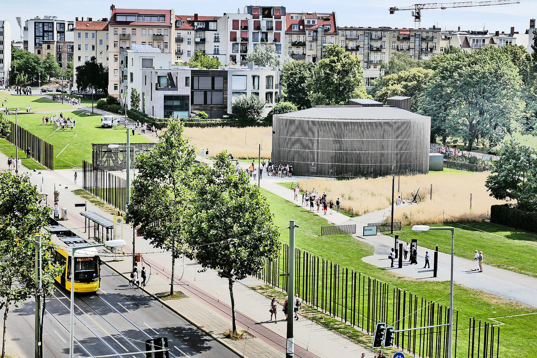 Eine gelbe Straßenbahn fährt entlang des Geländes der Gedenkstätte Berliner Mauer, das sich auf der linken Seite befindet, die Bernauer Straße hinab.