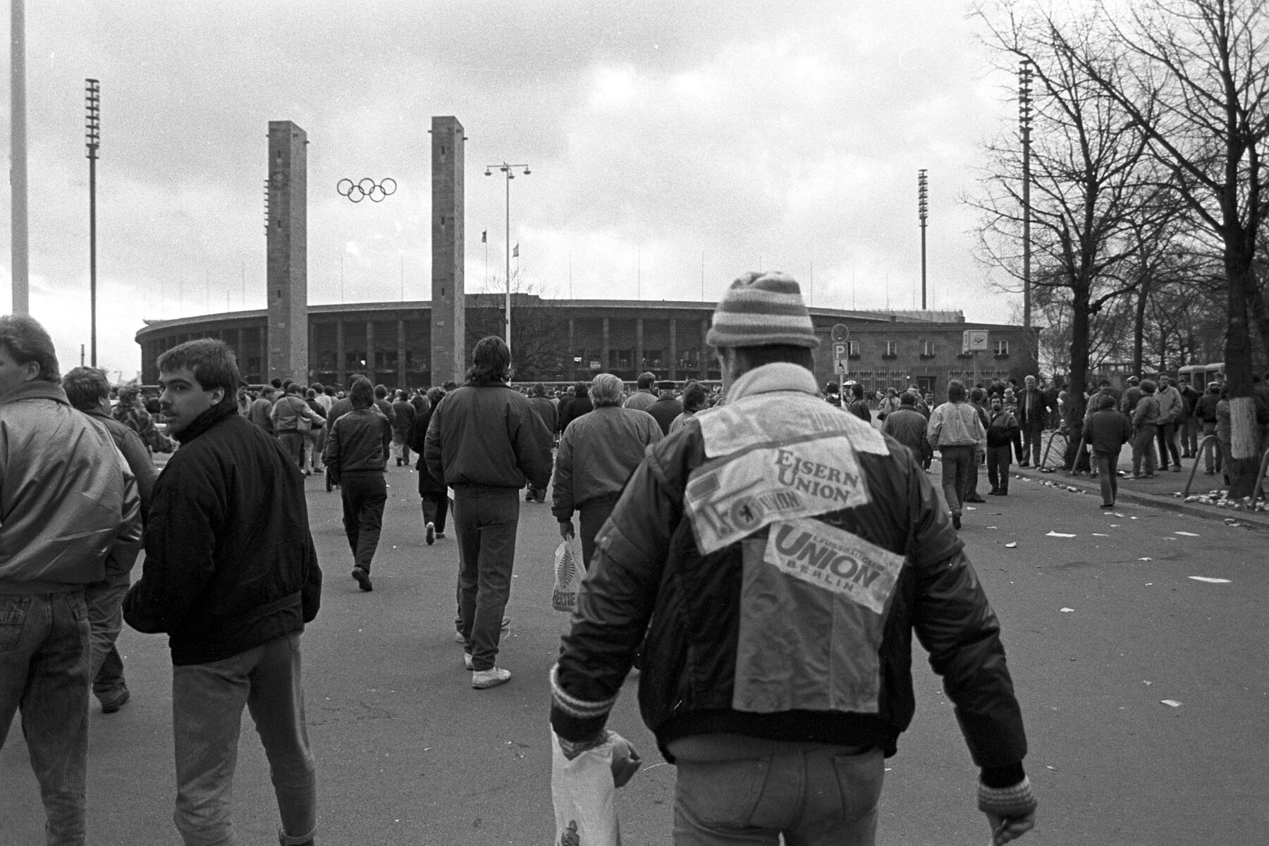 A Union fan with diverse patches on his jacket walks towards the Olympic Stadium.