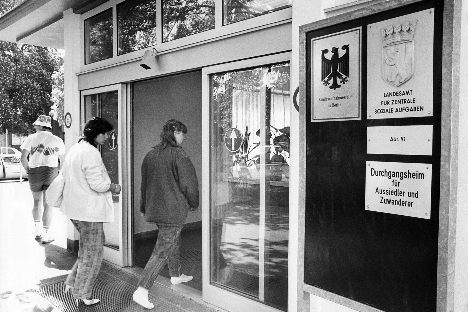 Two people walk through the entrance door of the Marienfelde Refugee Centre.