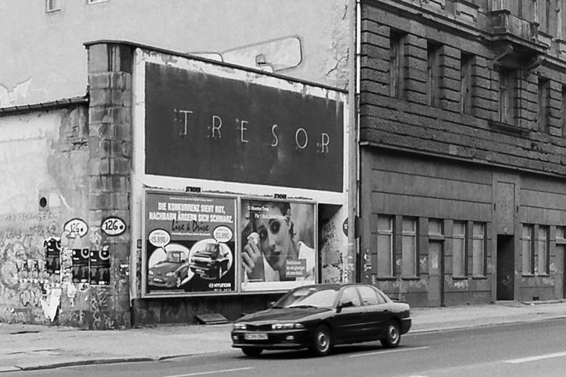 Car in front of the one-storey entrance to the safe club, with a multi-storey house to the right.