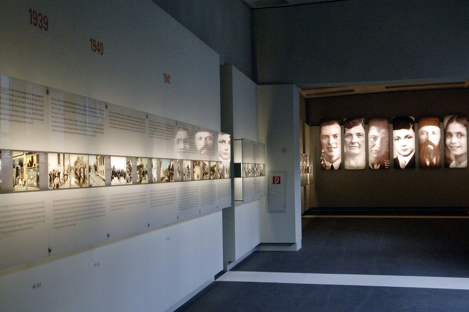 Wände im unterirdischen Ort der Information mit großen Porträts, kleinen Bildern und Texten.