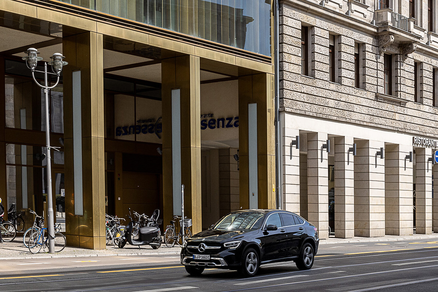 Car in front of a gold-coloured new building, with a multi-storey old house to the right.