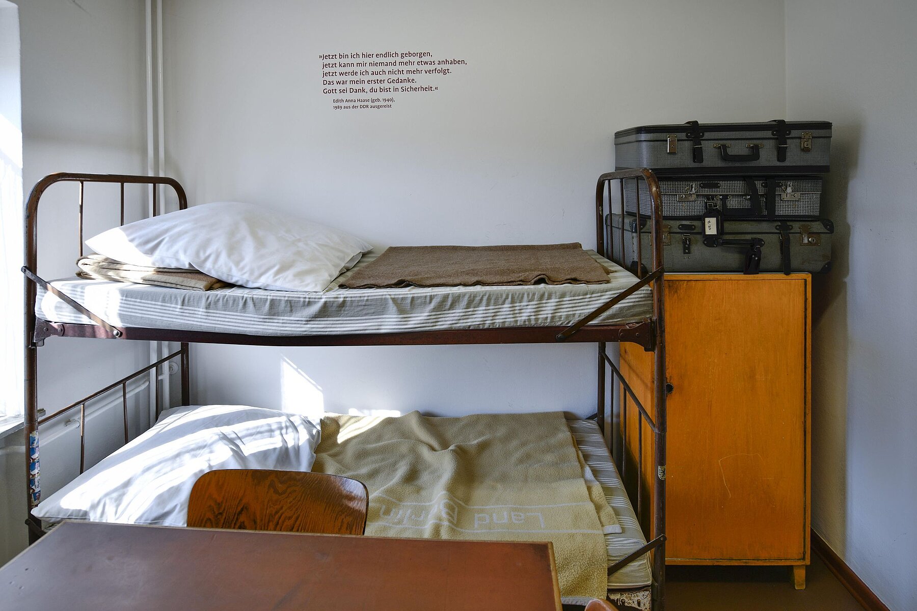 In one room there is a double bunk bed and to the right of it a wooden cupboard on which three suitcases lie.