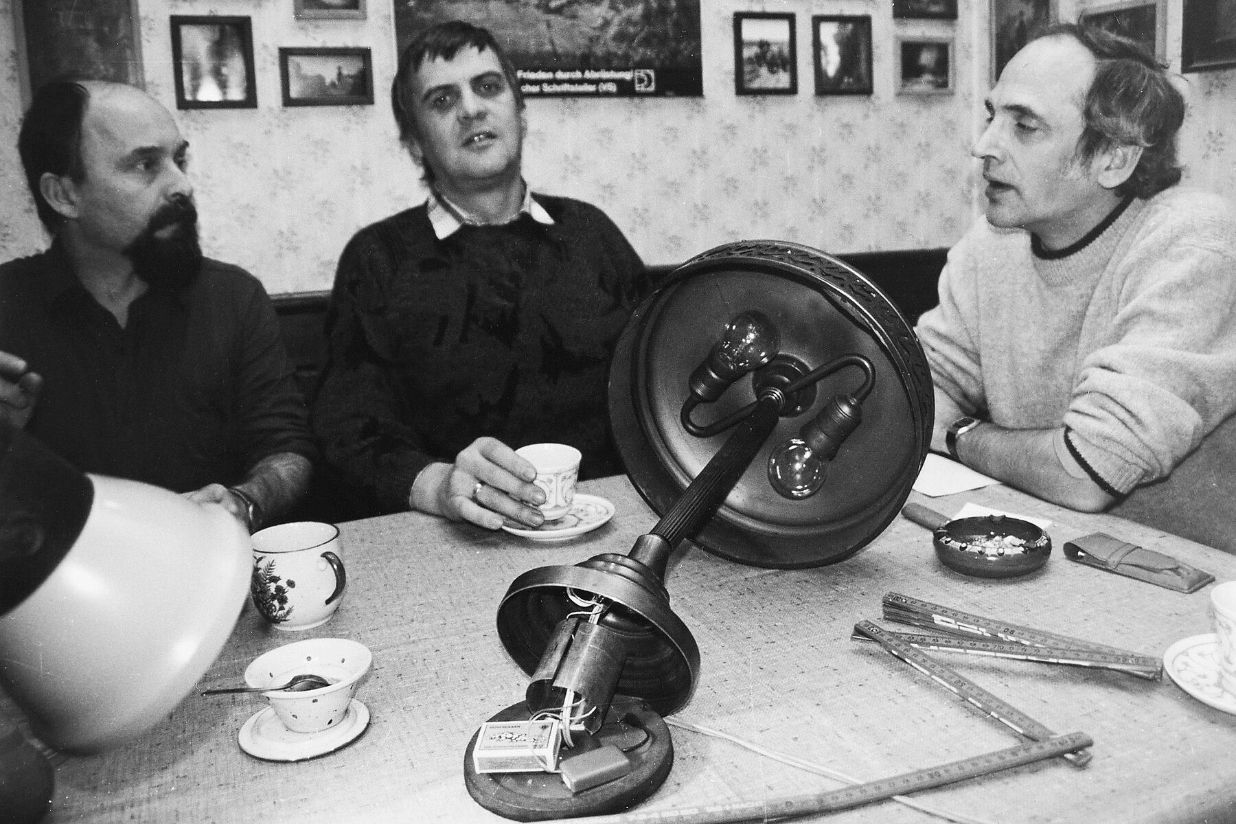 Pfarrer Rainer Eppelmann sitzt mit zwei westdeutschen Journalisten am Tisch, vor ihnen liegen mehrere Abhörmikrofone. 