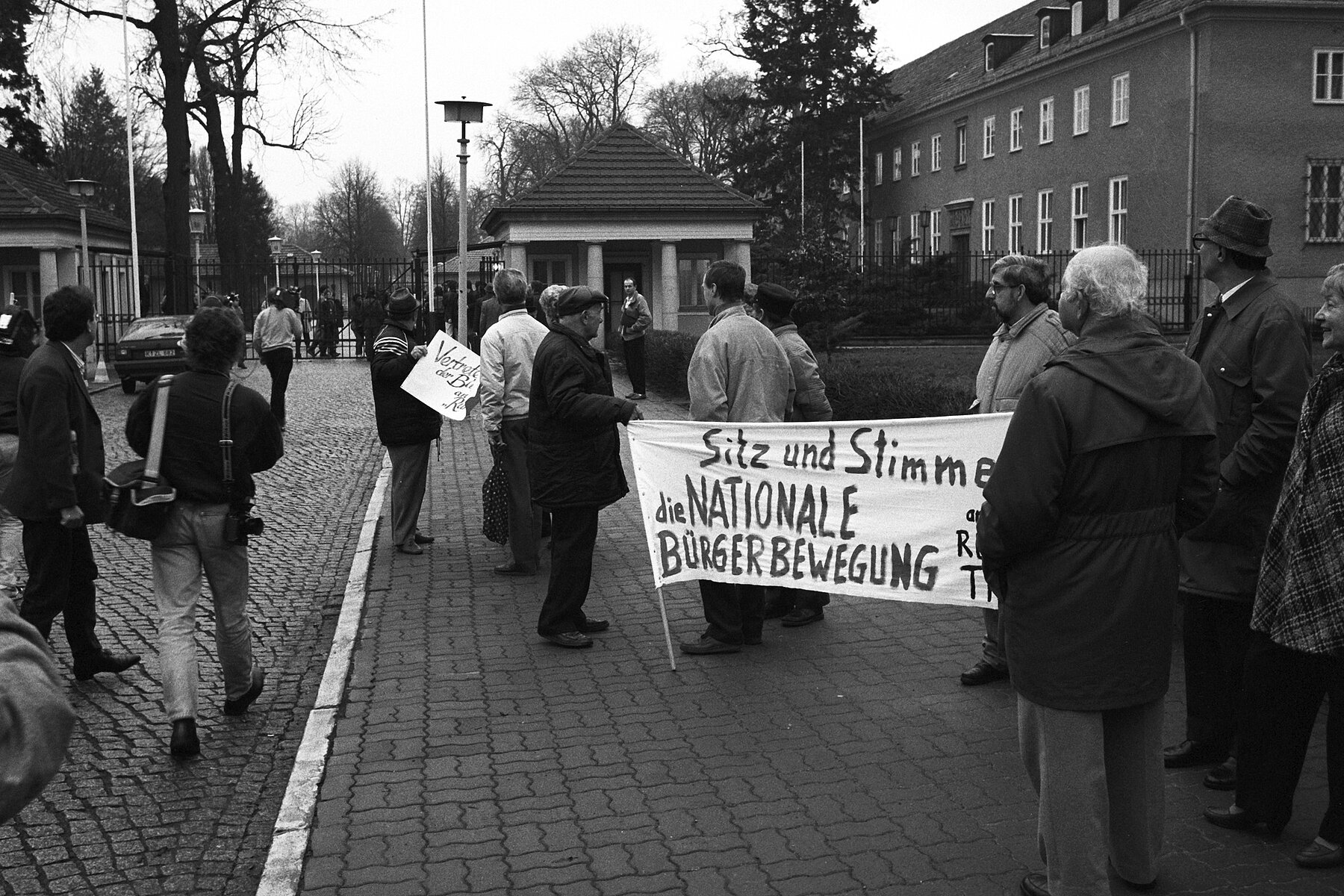 People with signs in front of the conference building of Schloss Schönhausen.