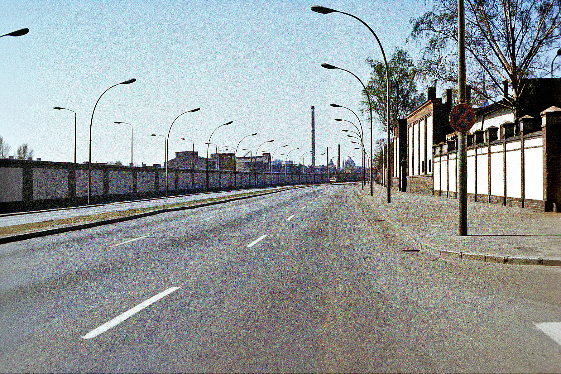 Straßenverlauf mit Grenzanlage. Viele Straßenlaternen stehen sowohl in Richtung Straße als auch in Richtung der Grenzanlage.