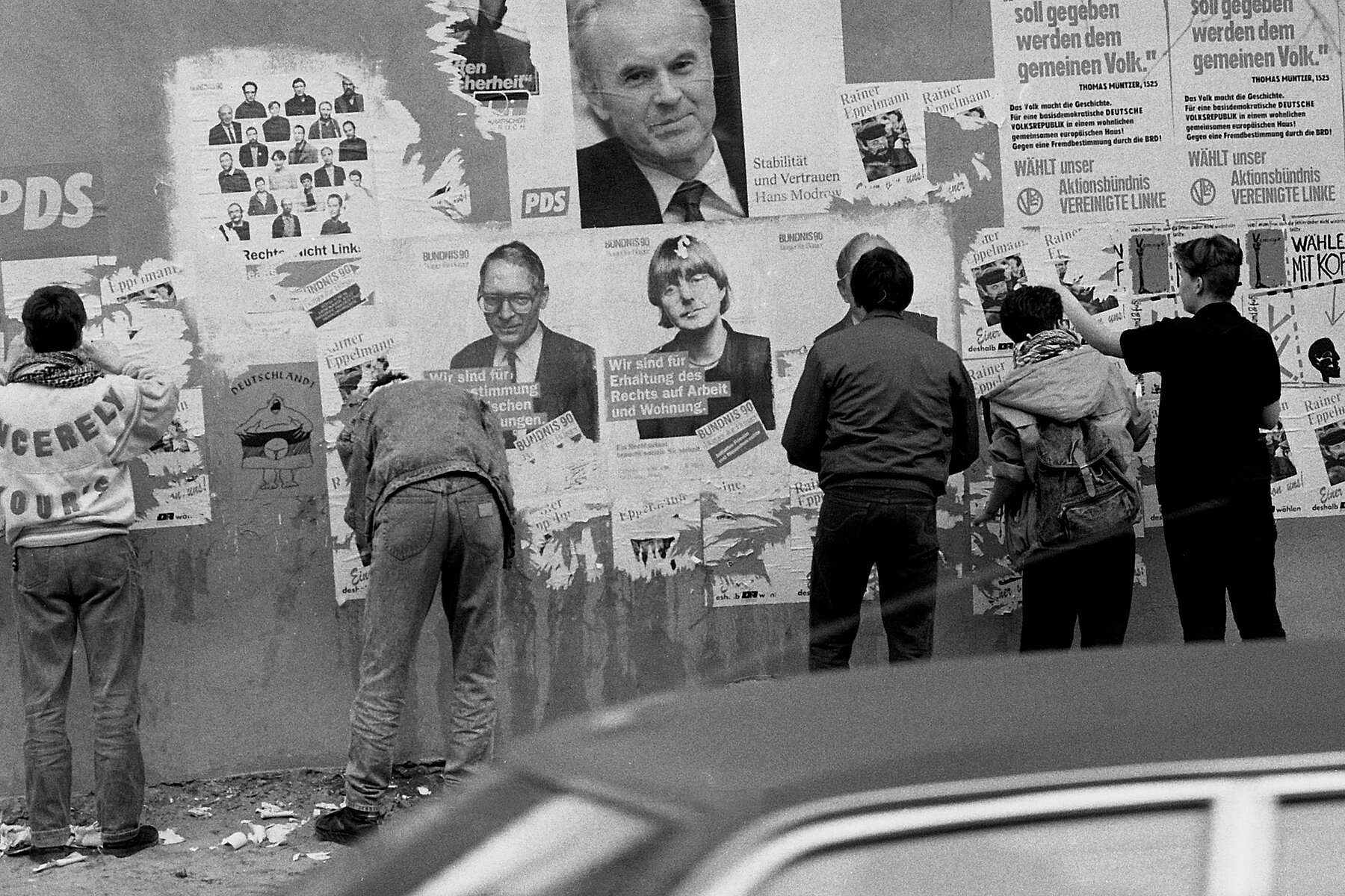 People in front of a wall with campaign posters of different political parties.