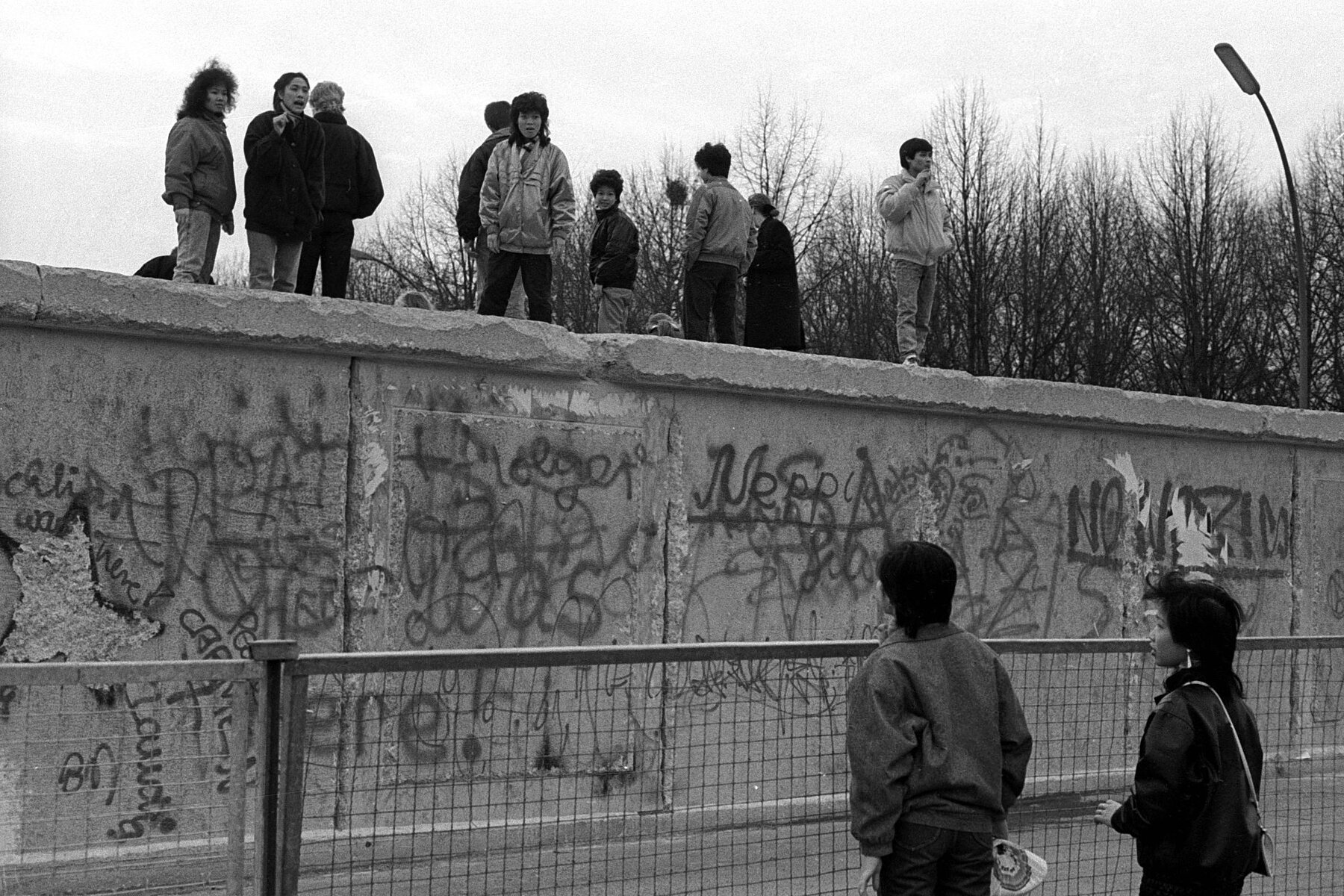View of the Berlin Wall with graffiti. On the wall are several Asian persons facing each other. 