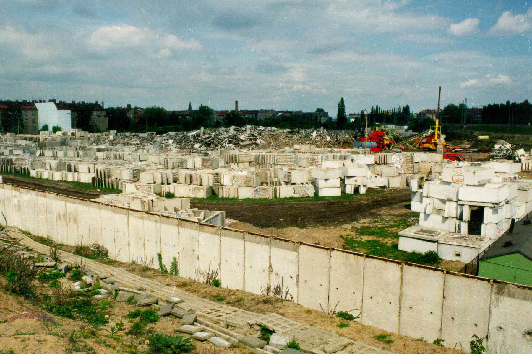 Parts of the Berlin Wall are stored on a piece of fallow land and shredded by a machine.