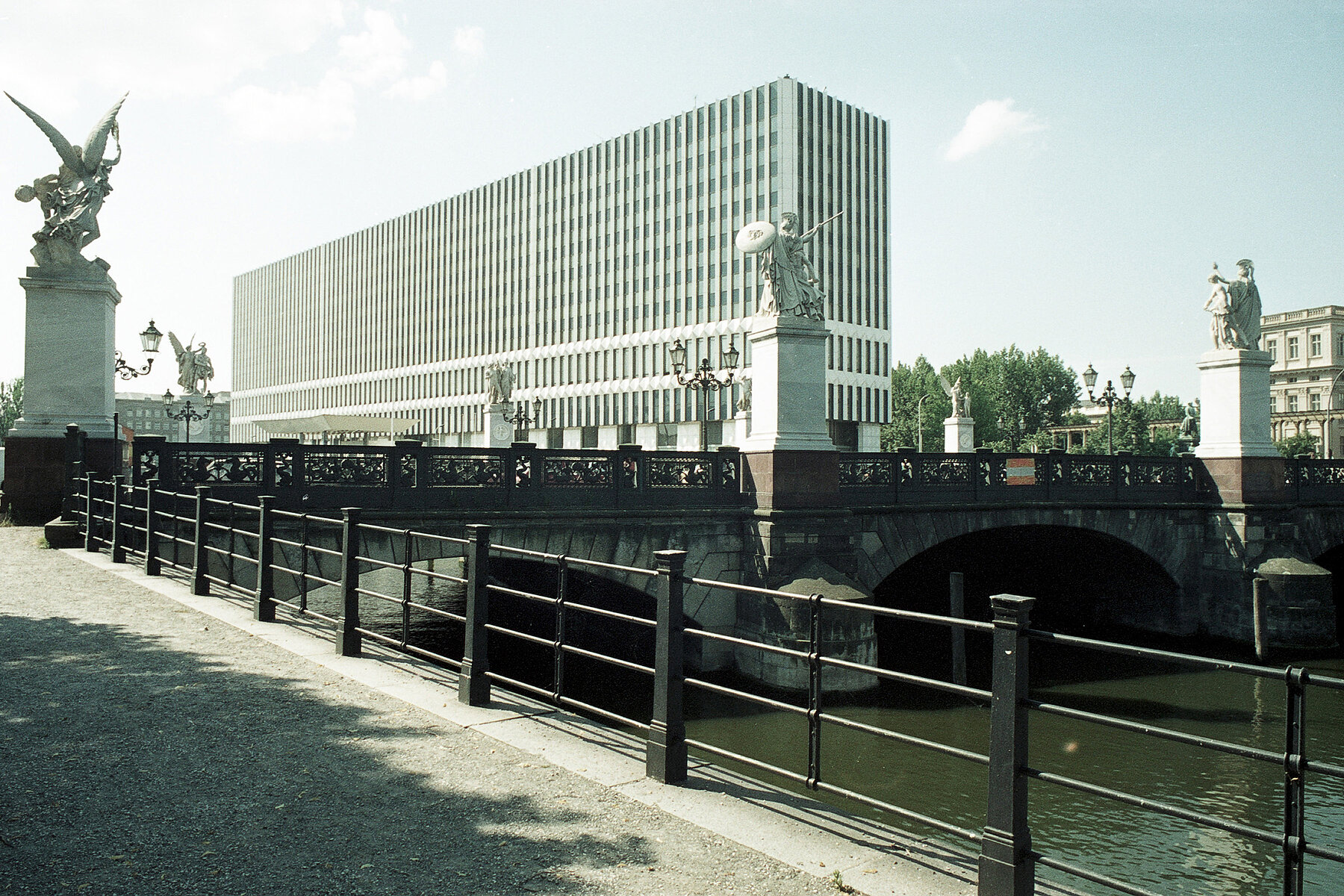 The Schlossbrücke crossing the Spree with sculptures of warriors and goddesses of victory on pedestals. In the background is the white high-rise building of the Ministry of Foreign Affairs of the GDR.