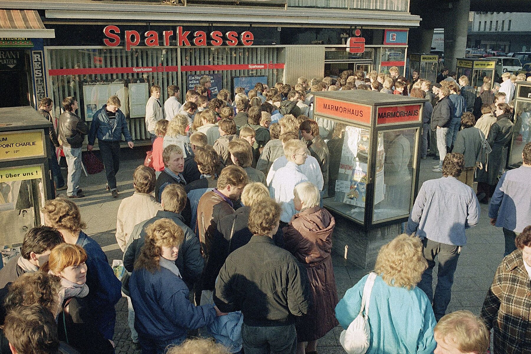 A long line of people in front of a Sparkasse. 