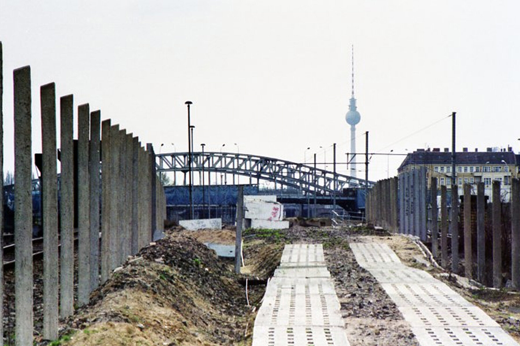 Ein Weg mit Lochplatten der ehemaligen innerdeutschen Grenzanlage in Richtung Bösebrücke. Rechts dahinter befindet sich der Fernsehturm.