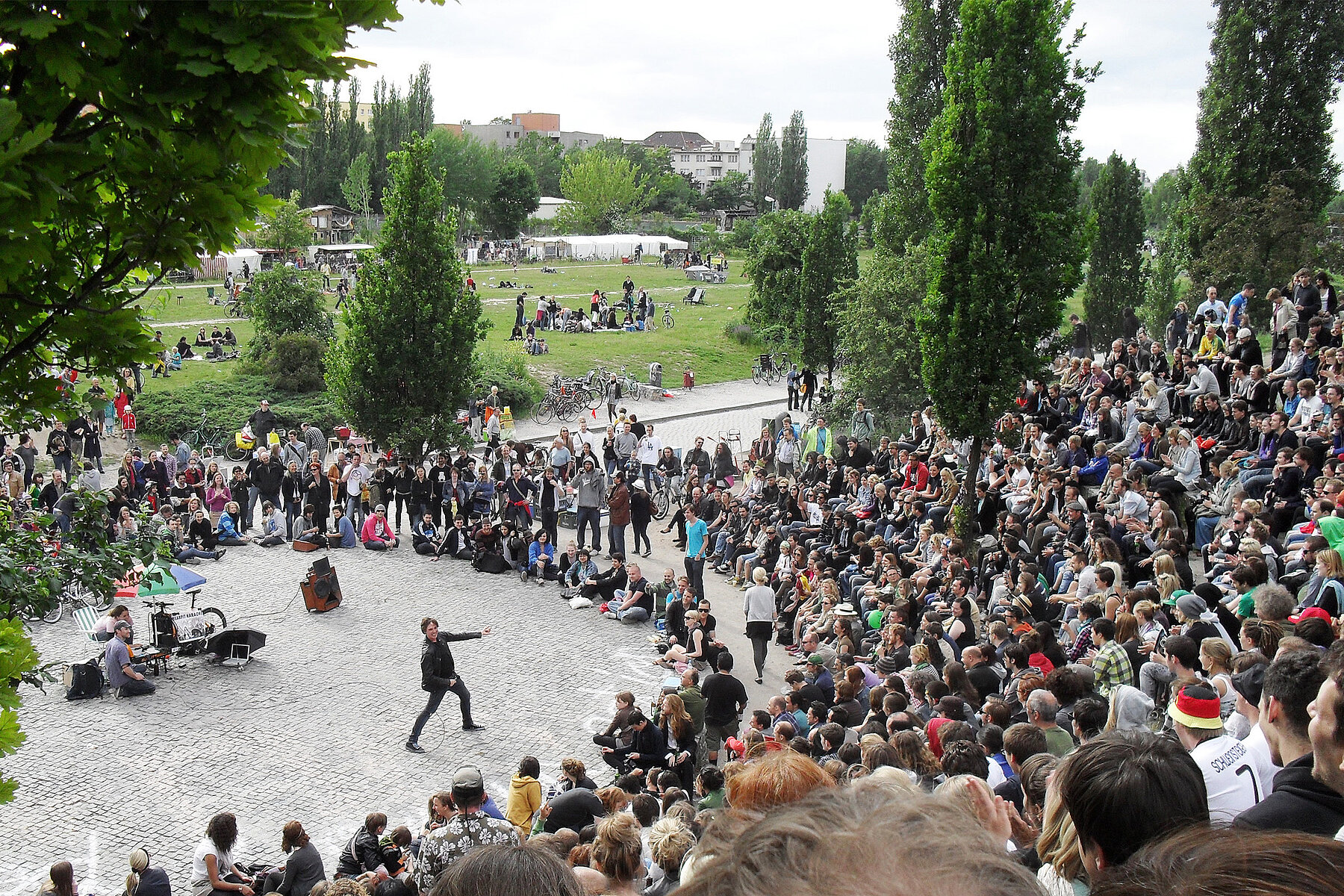 Many spectators in the amphitheatre of the Mauerpark watching a karaoke singer on the stage in the centre. 