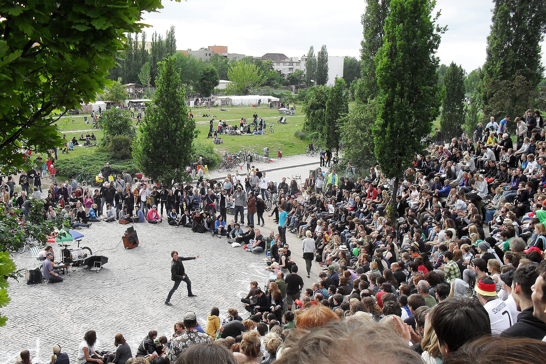 Im Amphitheater im Mauerpark sitzen viele Zuschauende und verfolgen einen Karaokesänger auf der Bühne in der Mitte. 