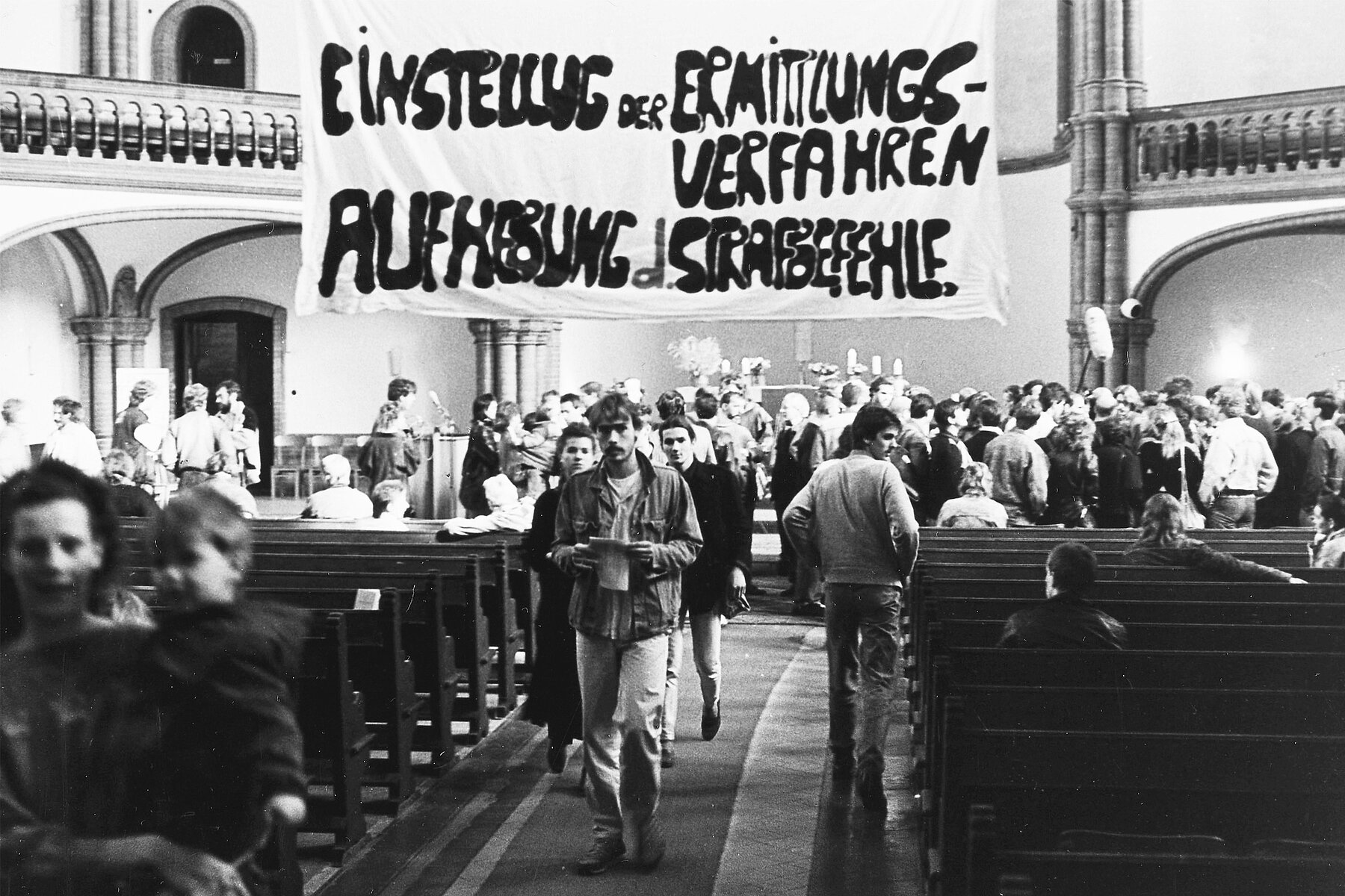 Menschenmenge vor dem Altar in der Kirche. Darüber hängt ein Banner mit der Aufschrift: Einstellung der Ermittlungsverfahren. Aufhebung der Strafbefehle.  