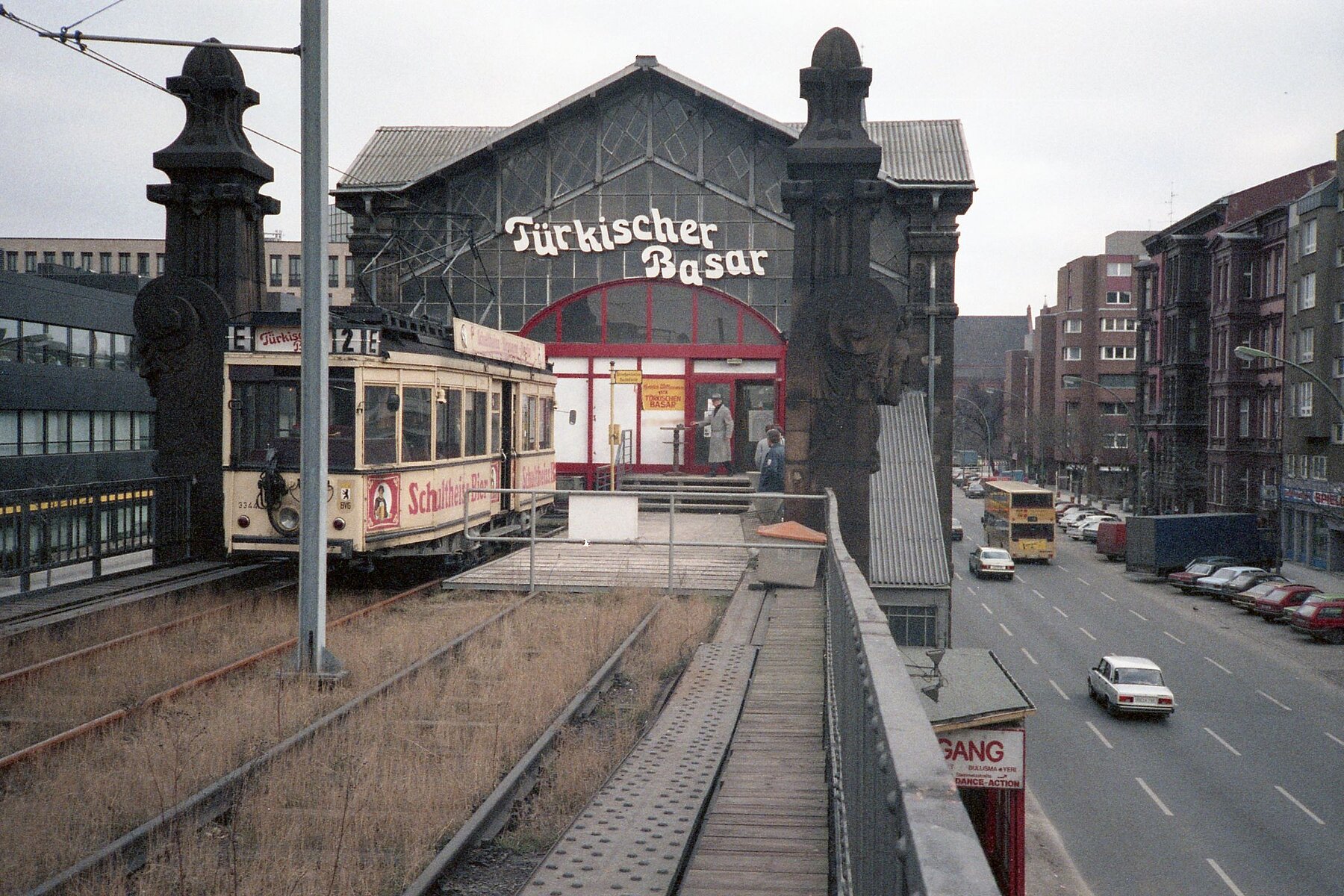 Der Hochbahnhof vom Gleisbettaus. Links im Bild die historische Straßenbahn. Über der roten Eingangstür hängt der weiße Schriftzug Türkischer Basar. 