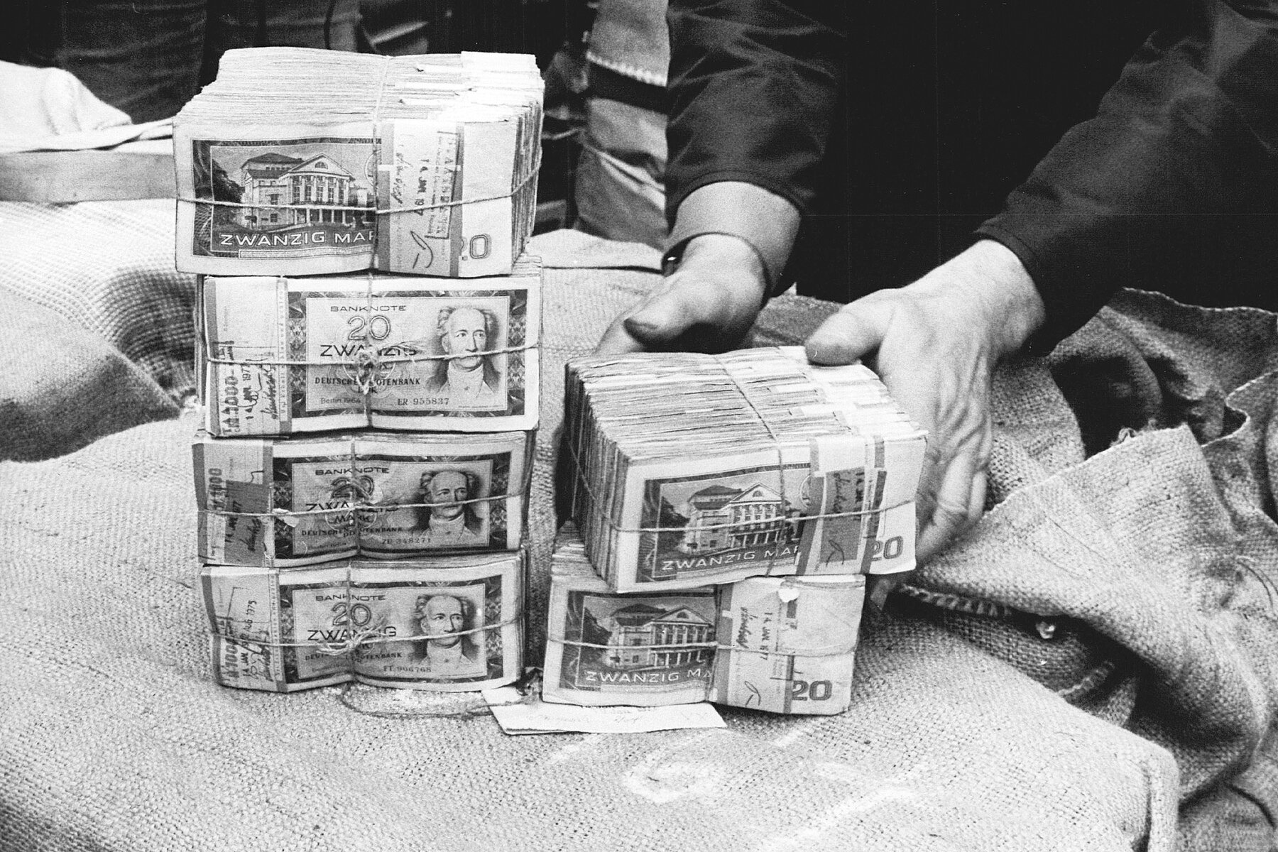 Six thick bundles of 20 GDR-Mark bills piled on a linen bag.