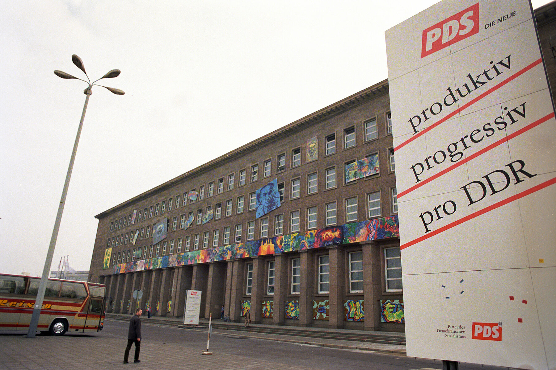 Vor dem Haus am Werderschen Markt steht ein großes Werbeplakat für die PDS. Darauf ist der Slogan produktiv, progressiv, pro DDR zu lesen.