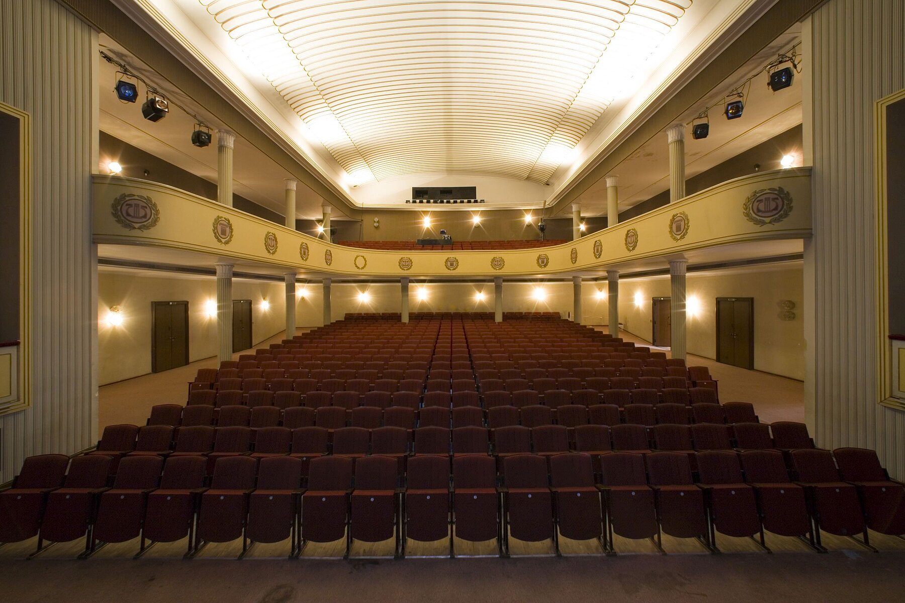 A theatre hall with a tier from the direction of the stage with dark red seating.
