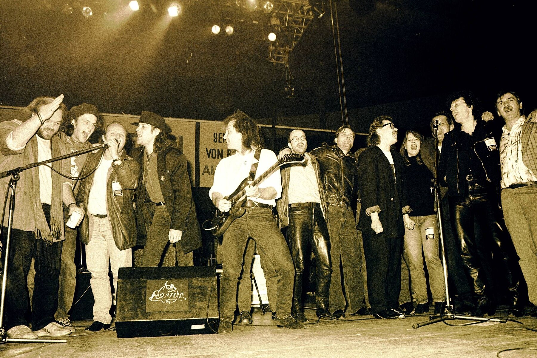 Twelve musicians singing in front of two microphones in a row on a stage. 