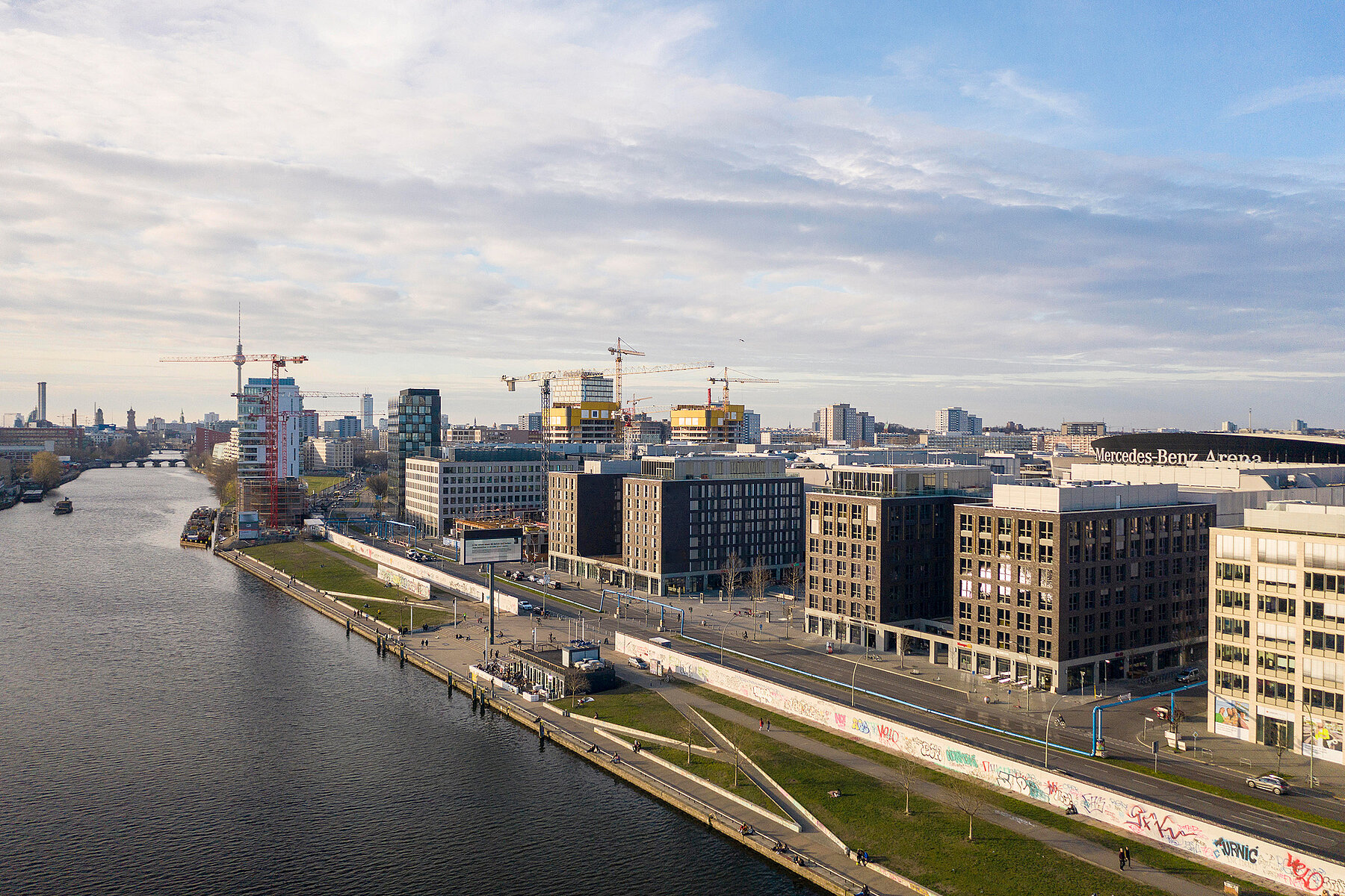 Links die Spree, rechts das Ufer mit der East Side Gallery und mehreren Neubauten dahinter.